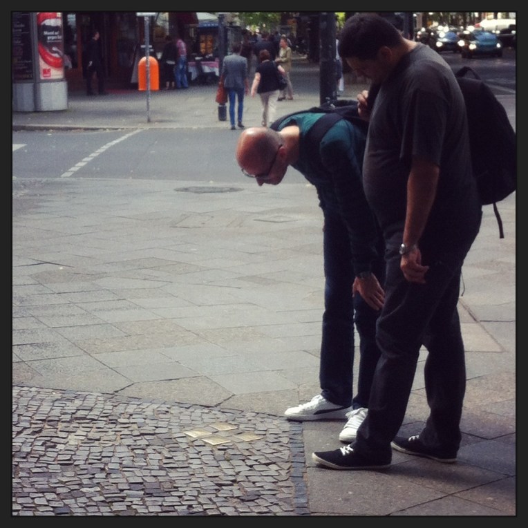 Pedestrians bow to look at Stolpersteine in West Berlin